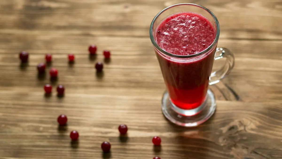 Photo rapprochée d'un verre de jus de cranberry avec canneberges rouges et feuilles vertes